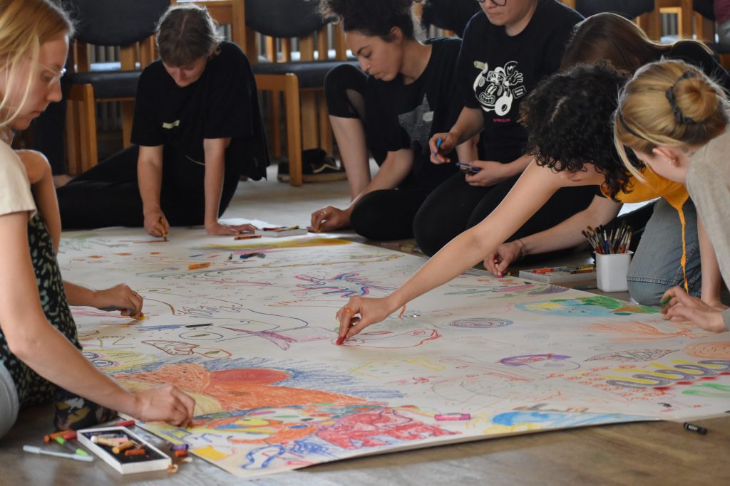 A large group drawing together on a big sheet of paper on the floor