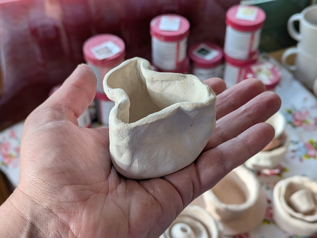 A hand holding a pinched clay pot