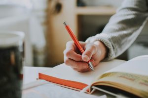 Close-up of a hand writing in a notebook with a red pen