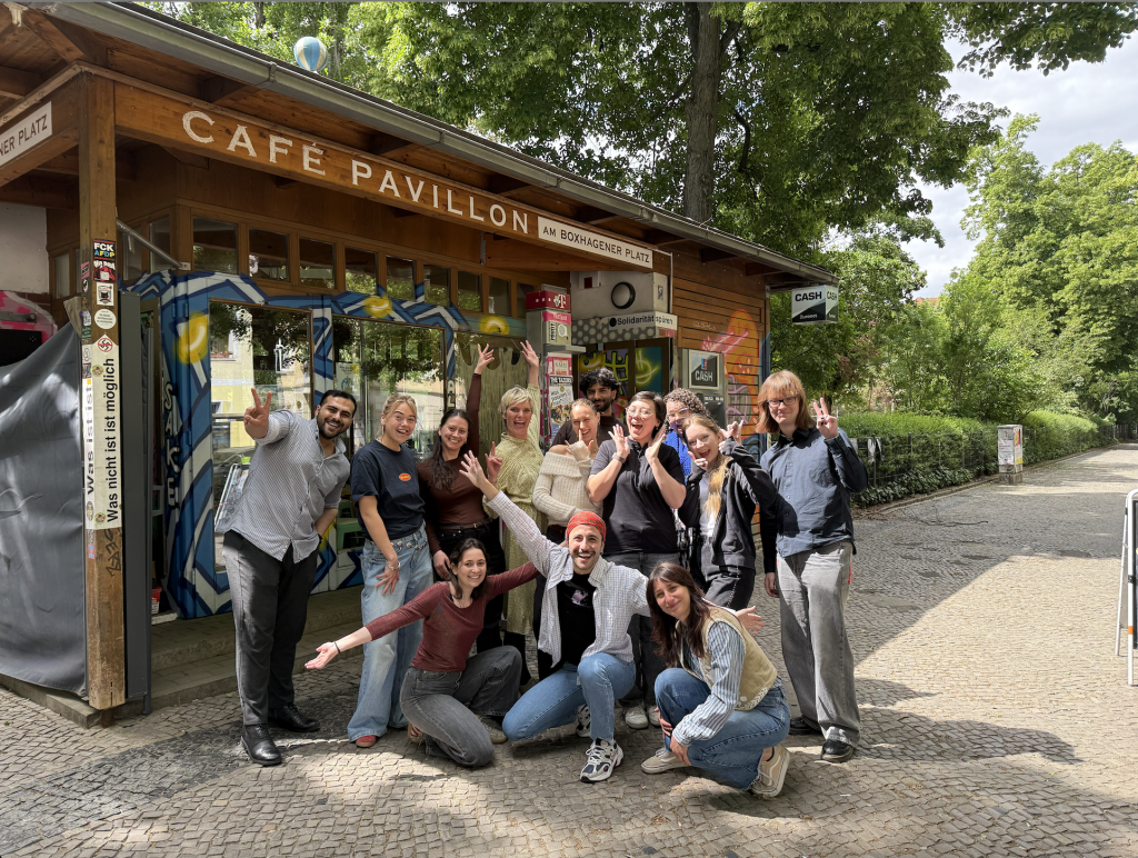 ForEvyone Team outside Café Pavillon, a wooden kiosk café at Boxhagener Platz, with trees and a cobblestone street around them